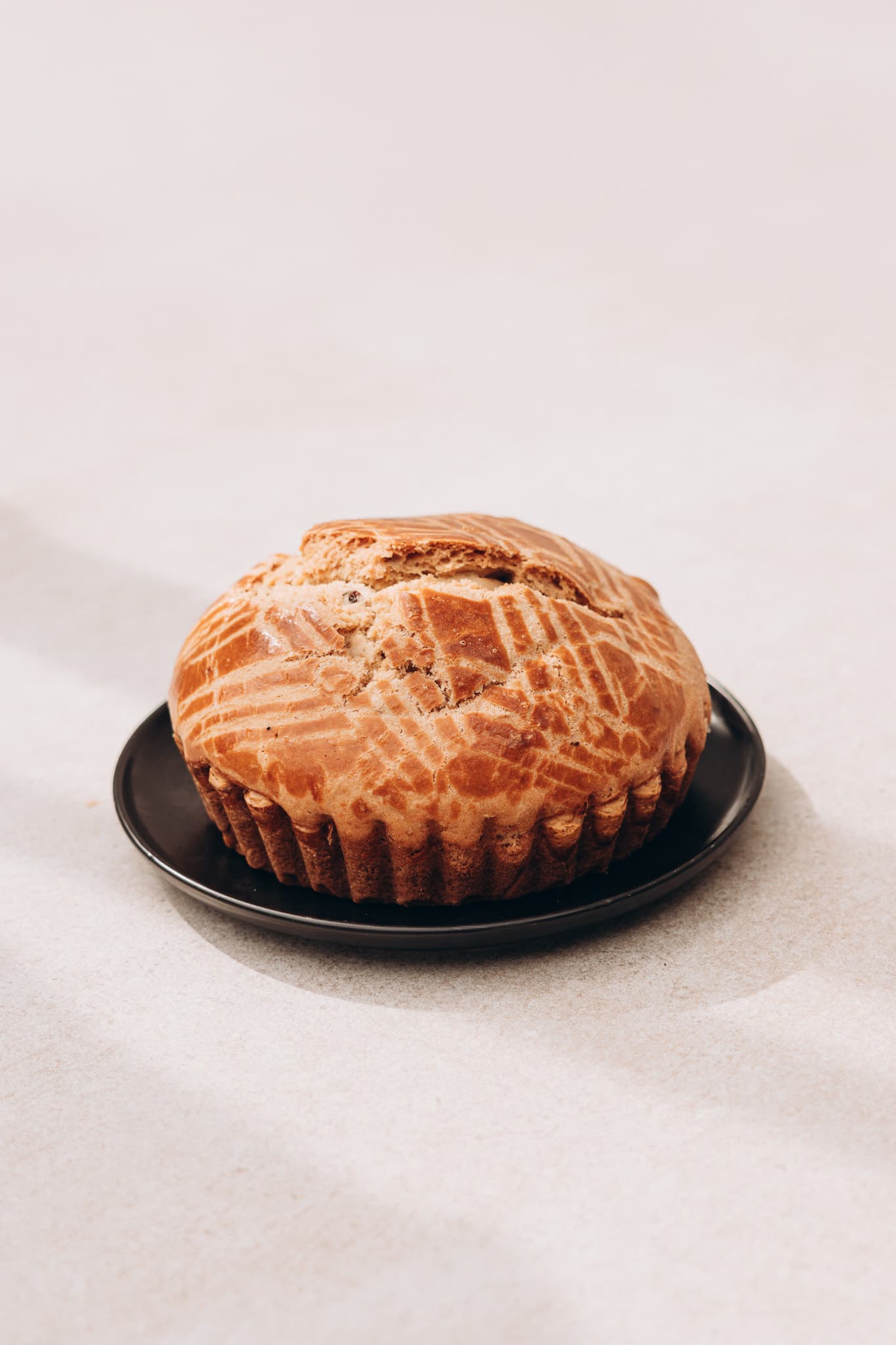 Un Kouign des Gras doré, au dessus quadrillé, posé sur une assiette noire